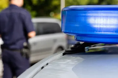 Błyskawica policyjnego radiowozu na tle mundu funkcjonariusza i zaparkowanego samochodu.