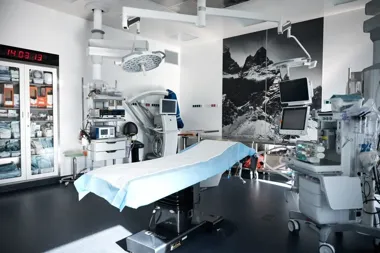 Nowoczesna, pusta sala operacyjna z łóżkiem chirurgicznym, lampami operacyjnymi, monitorami i szafą z medycznymi materiałami eksploatacyjnymi.